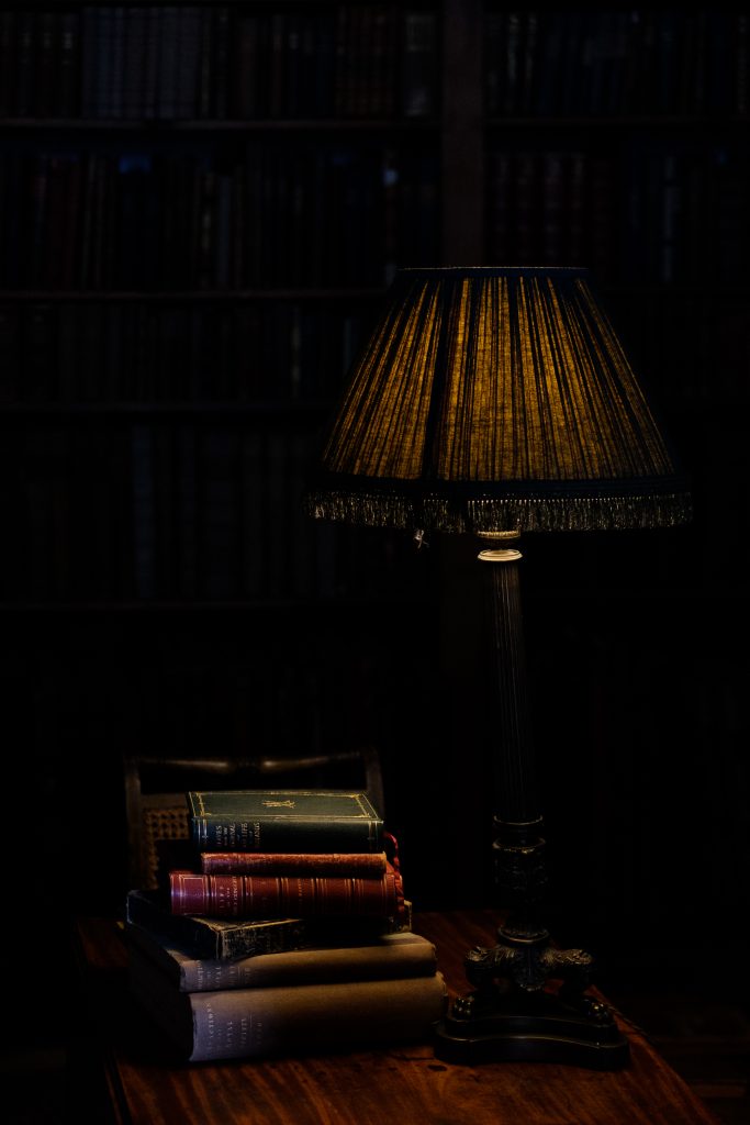 Lamp and books on a side table, dark and moody.
