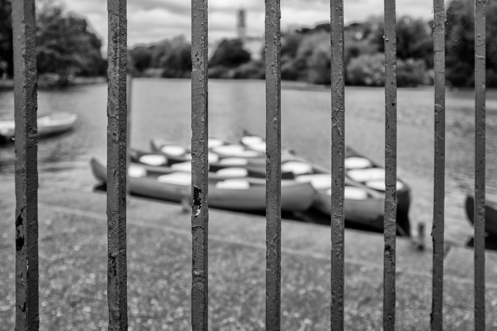 Small boats at the bank of Highfields Lake, Nottingham viewed through railings.