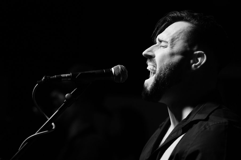 Black and white photo of Tom Webster on guitar and vocals.